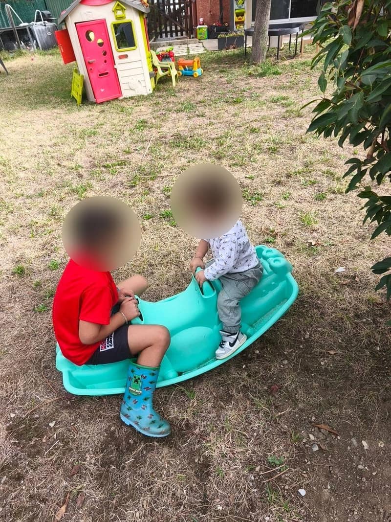 Deux garçons, visages floutés, jouent sur une bascule dans le jardin de l'assistante maternelle à Espinasses